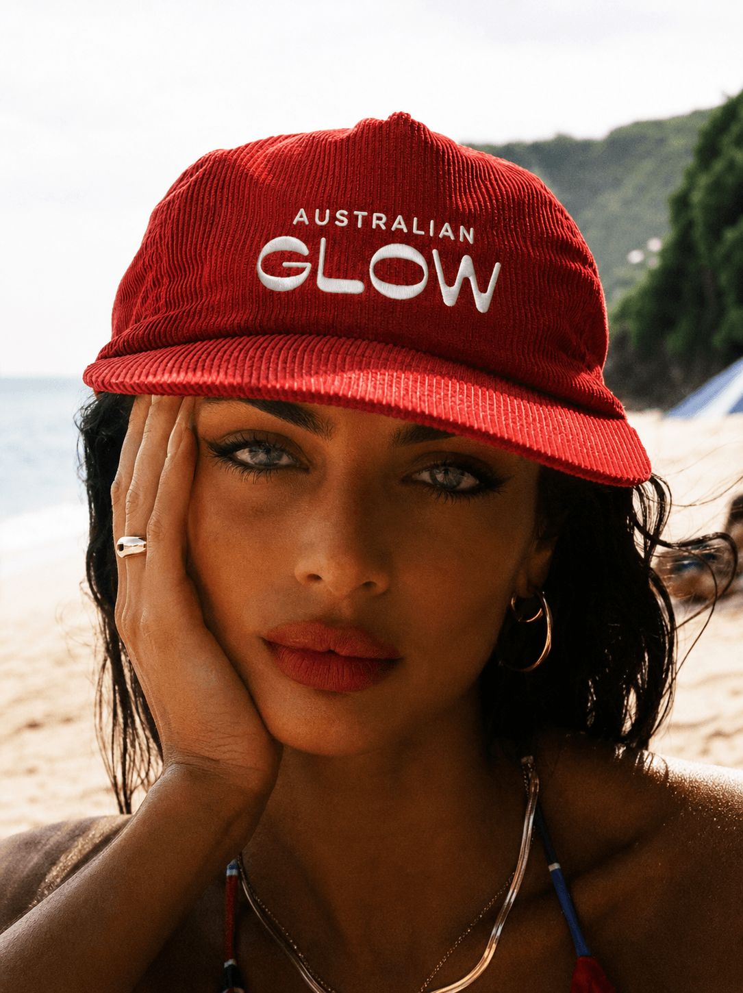 Australian Glow merch — model in red AG cap on the beach