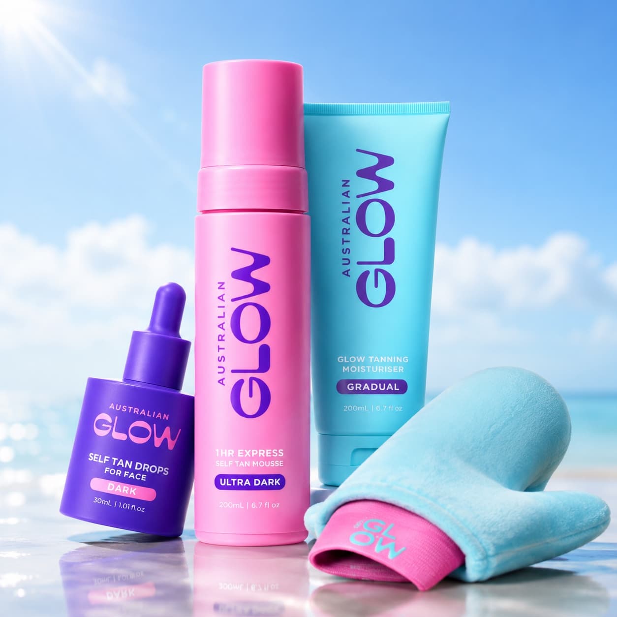 The Main Character contents on the beach — Face Tan Drops, Ultra Dark mousse, Gradual Tanning Moisturiser and the blue applicator mitt