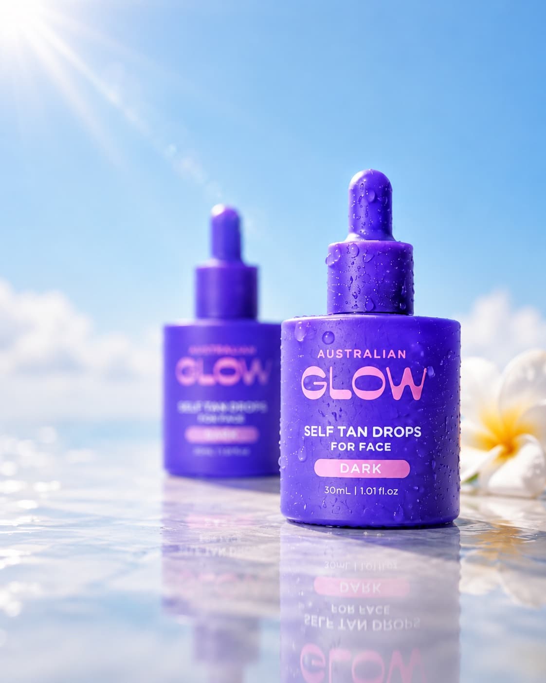 Face Tan Drops bottles with a frangipani flower against a summer sky