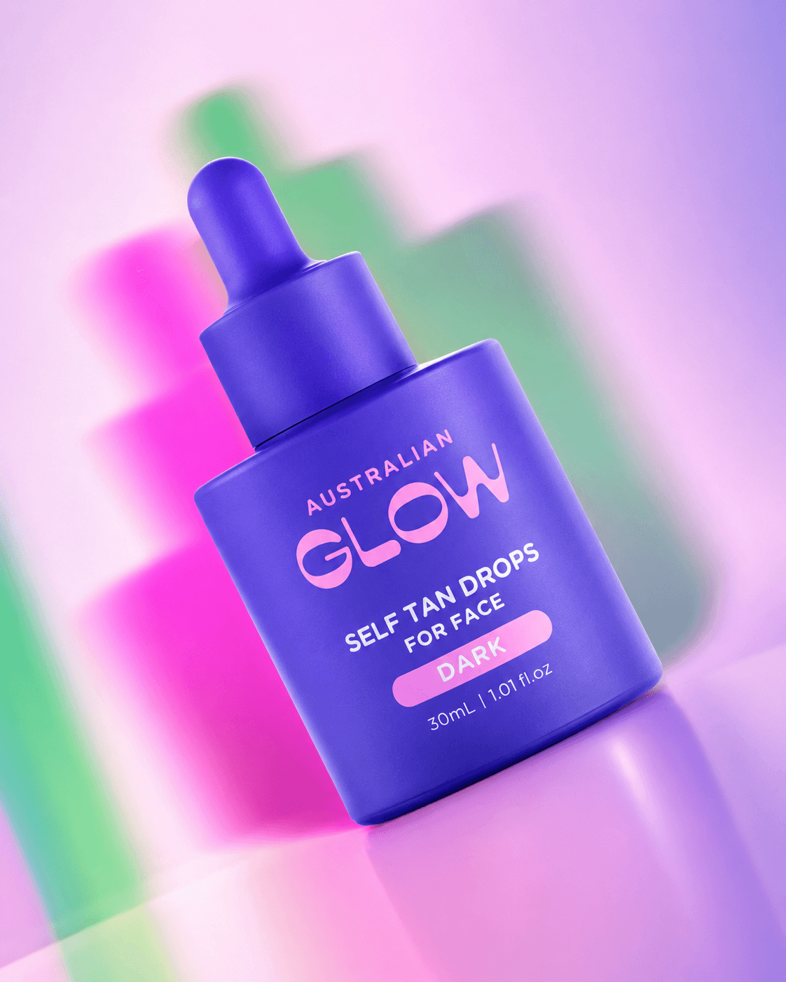 Face Tan Drops Dark — single bottle floating on a holographic pink, green and lilac gradient