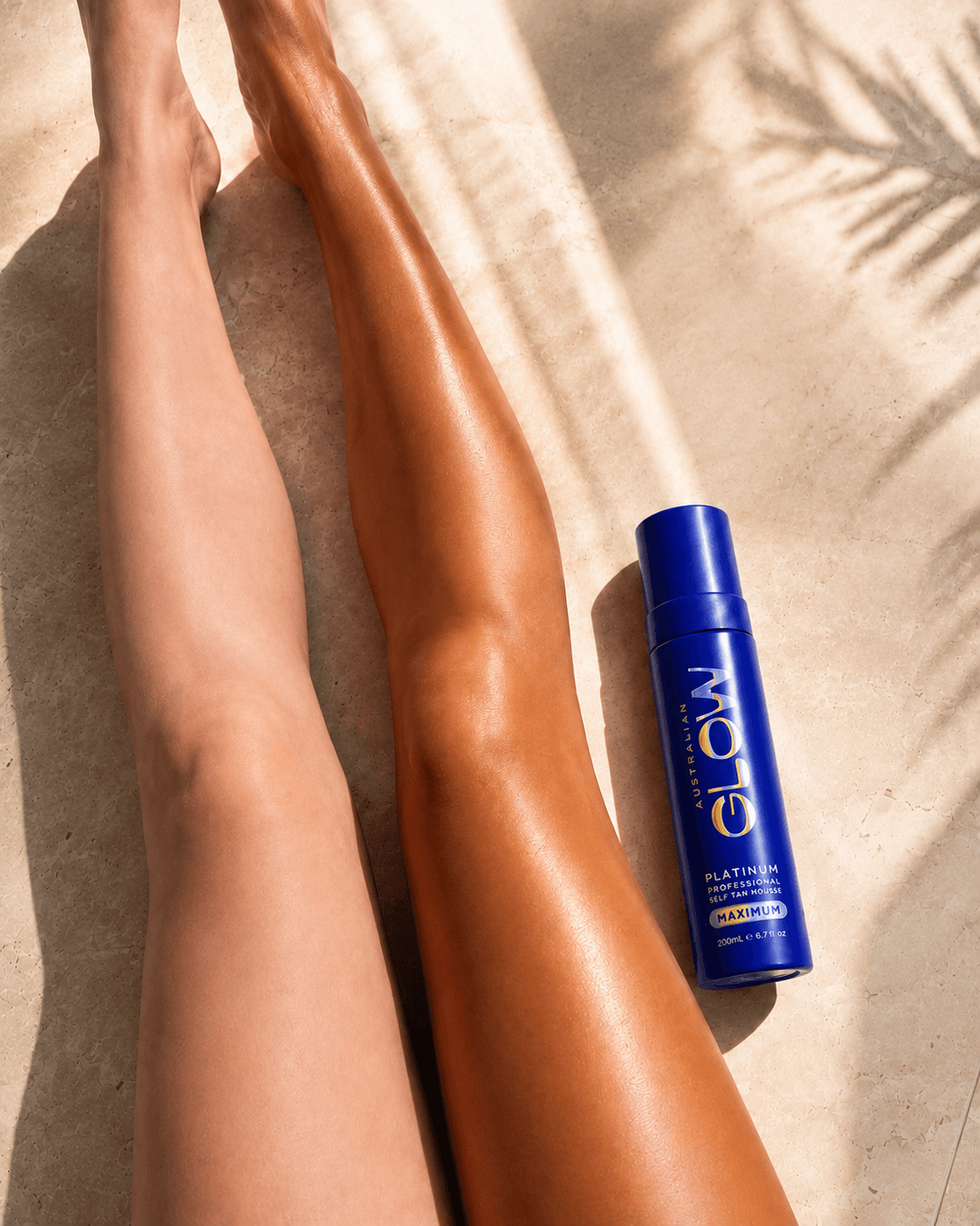 Australian Glow Platinum — tanned legs on warm sand with a palm-frond shadow